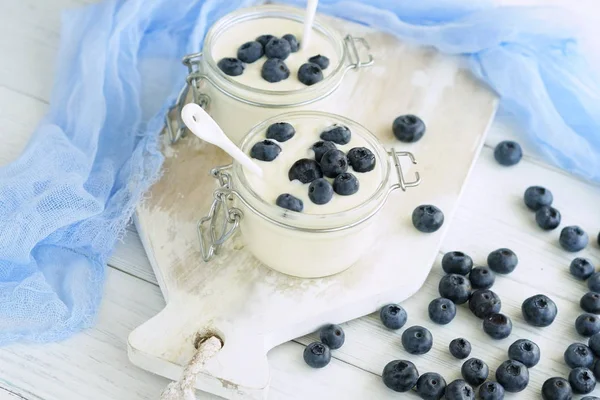 Un delicioso y saludable desayuno de yogur fresco con arándanos en un pequeño frasco de vidrio sobre un fondo de madera blanca . — Foto de Stock