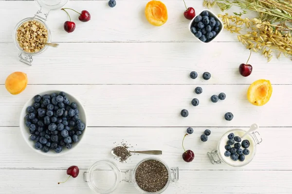 Un petit déjeuner savoureux et sain composé de bleuets frais, de granulés, de graines de chia, de yaourt aux bleuets dans un bocal en verre sur un fond de bois blanc. — Photo