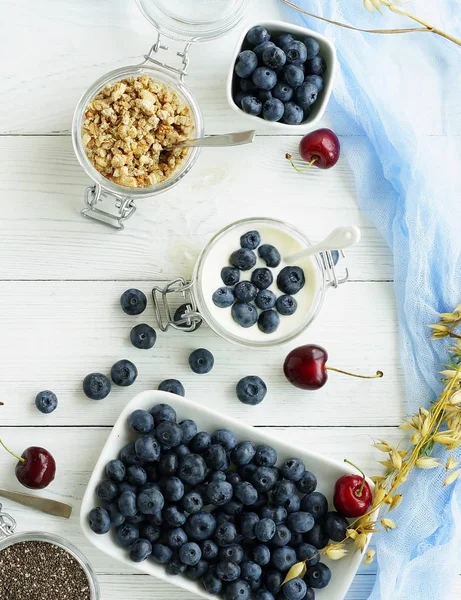 En god och hälsosam frukost med färska blåbär, granulat, chiafrön, yoghurt med blåbär i en glasburk på en vit trä bakgrund. Ovanifrån — Stockfoto