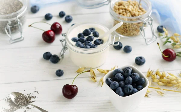 Ein leckeres und gesundes Frühstück mit frischen Blaubeeren, Granulat, Chiasamen, Joghurt mit Blaubeeren in einem Glas auf weißem Holzgrund. — Stockfoto
