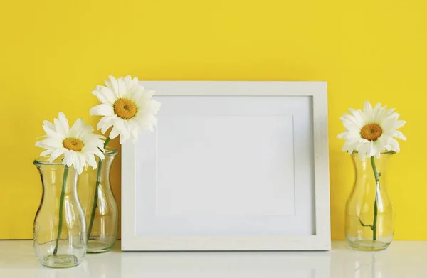 Modèle de cadre blanc avec des fleurs de camomille dans des vases sur un fond jaune. Espace de copie — Photo