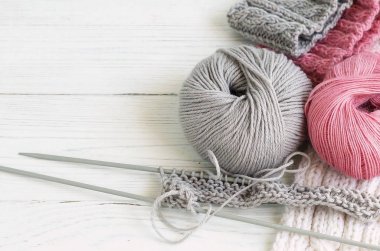 Gri ve pembe örgü yünü ve beyaz ahşap arka planda örgü iğneleri. Üst görünüm. Boşluğu kopyala