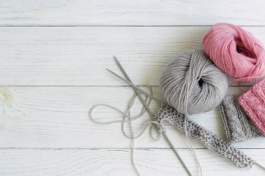 Gri ve pembe örgü yünü ve beyaz ahşap arka planda örgü iğneleri. Üst görünüm. Boşluğu kopyala