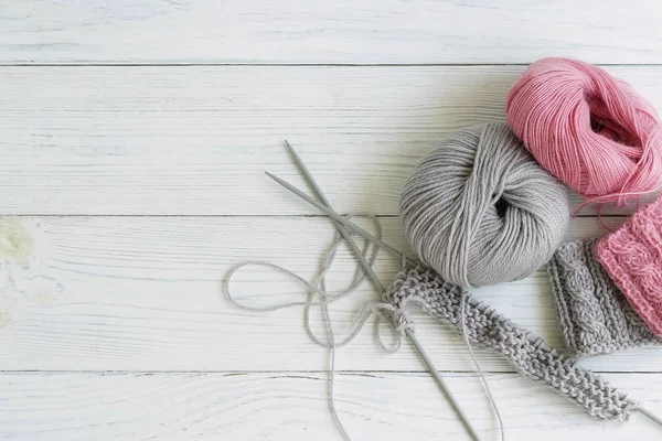 Gri ve pembe örgü yünü ve beyaz ahşap arka planda örgü iğneleri. Üst görünüm. Boşluğu kopyala