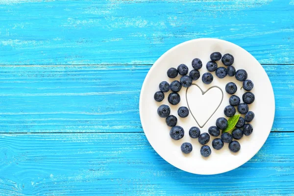 Arándanos frescos en un plato blanco con corazones sobre un fondo de madera azul. Vista superior. Copiar espacio — Foto de Stock