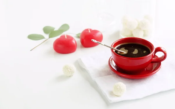Xícara vermelha com café, duas velas-coração e um ramo de eucalipto — Fotografia de Stock