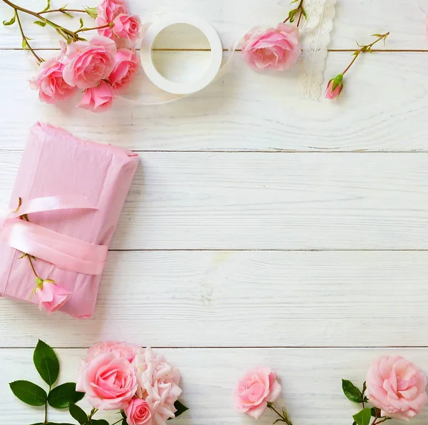 Bouquet of beautiful pink roses and gift in pink packing on white wooden background.Top view.Copy space