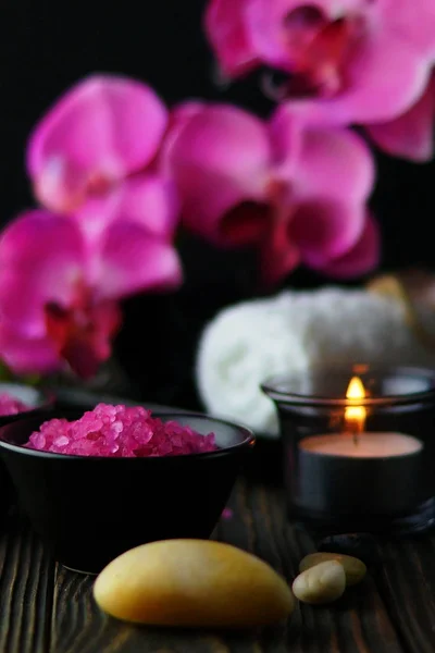 Composition of spa treatment on dark wooden background. Pink massage sea salt and orchids. Close up