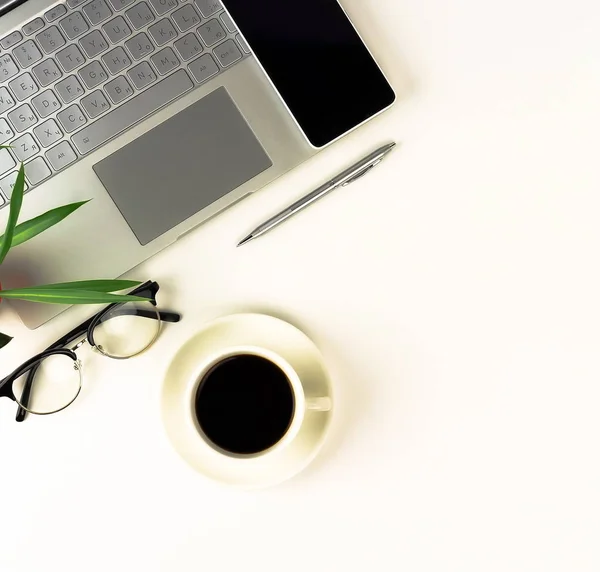 Top view of white office table with laptop, smartphone, cup of coffee and supplies. Top view with copy space.Flat lay