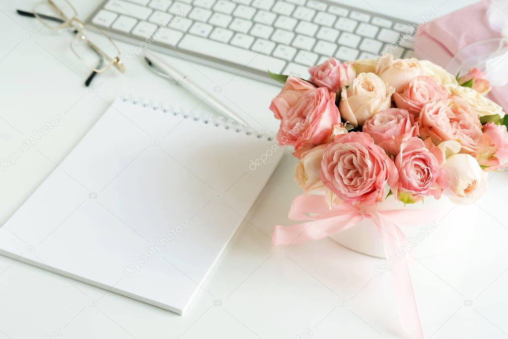 Office feminine desk, female accessories, workspace with laptop,  notebook and bouquet beautiful pale pink roses. Holidays concept.Copy space