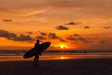 Bir plaj Bali günbatımı bakan bir sörfçü