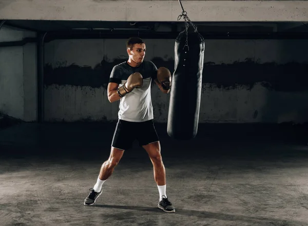 Mężczyzna ćwiczy boks na wielkiej czarnej torbie w garażu — Zdjęcie stockowe