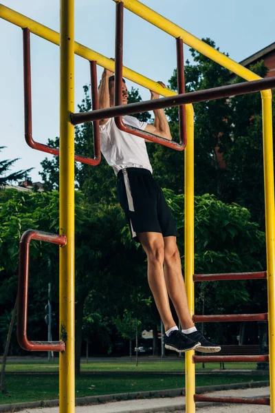 Muscular man doing pull-ups on horizontal bar in urban park — ストック写真