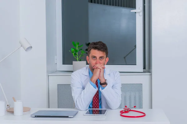 Männliche ernsthafte kaukasische Arzt sitzt in seinem Büro allein und th — Stockfoto