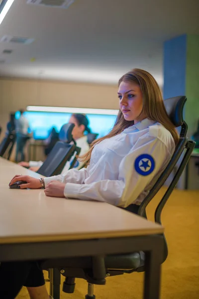 Female security guard sitting and monitoring modern CCTV cameras in a surveillance room.