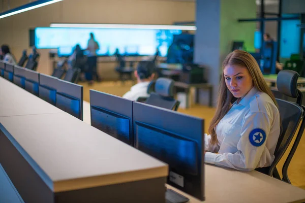 Female security guard sitting and monitoring modern CCTV cameras in a surveillance room.