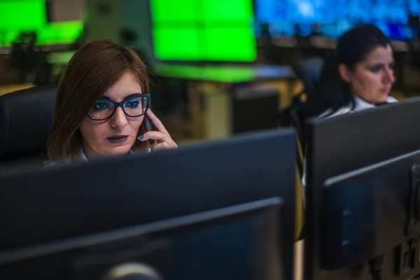 Female security guard sitting and monitoring modern CCTV cameras in surveillance room, talking on a cellphone.