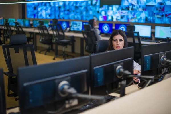 Female security guard sitting and monitoring modern CCTV cameras in surveillance room.