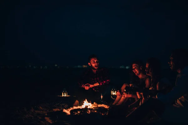 İnsanlar geceleri sahilde parlak bir şenlik ateşi etrafında oturup — Stok fotoğraf