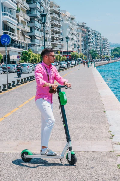Стильний чоловік їде своїм електронним скутером біля моря в сонячний день . — стокове фото