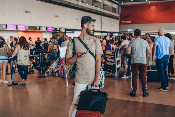 Mężczyzna z bagażem czeka w holu lotniska na swój samolot — Zdjęcie stockowe