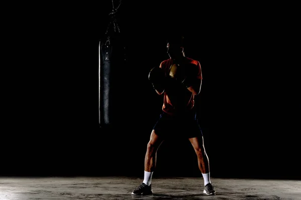 Silhouette male boxer hitting a huge punching bag at a boxing studio. Man boxer training hard