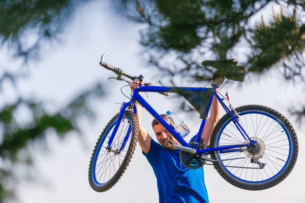 Egy erős férfi hegyi motoros felemeli a biciklijét, miközben mosolyog.. — Stock Fotó