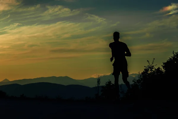 Tiro de esportivo jovem silhueta homem correndo na estrada da montanha em — Fotografia de Stock