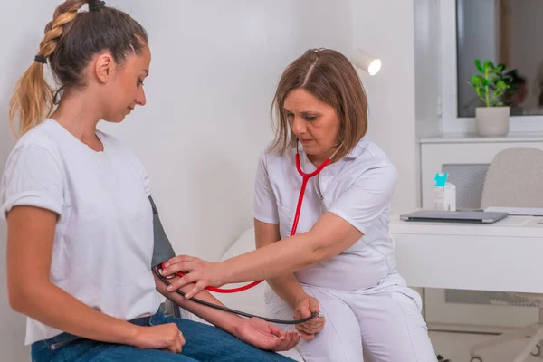 Médico femenino midiendo la presión arterial de su joven adolescente —  Fotos de Stock