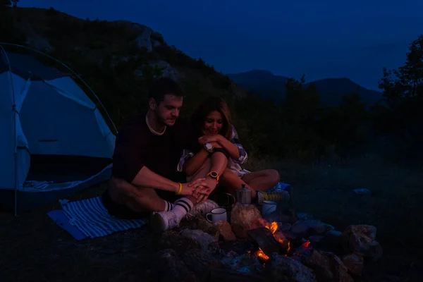 Genç çift kamp ateşinde dinleniyor ve kahve içiyorlar. — Stok fotoğraf