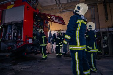Firefighters preparing their uniform and the firetruck in the ba clipart