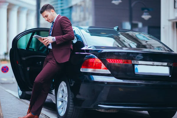 Joven Hombre Negocios Guapo Apoyado Limusina Sonriendo Mientras Mira Teléfono — Foto de Stock