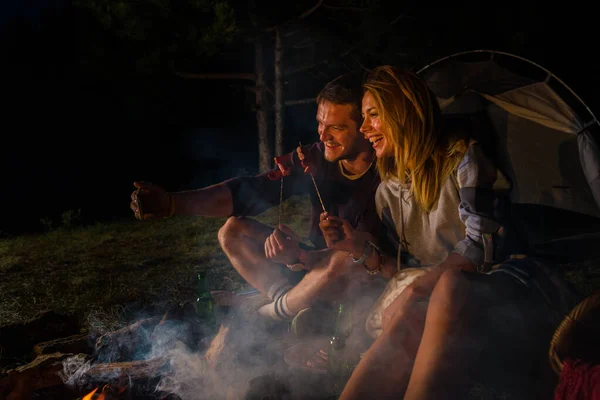 Junges Paar backt Würstchen am Lagerfeuer und trinkt Bier — Stockfoto