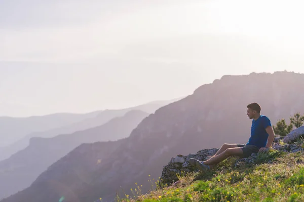 Hombre aventurero sentado en la cima de una montaña y disfrutando del ser — Foto de Stock