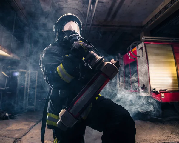 Portrait of a female firefighter wearing a helmet and all safety equipment a while holding a tomahawk and wearing an oxygen mask indoors surrounded by smoke