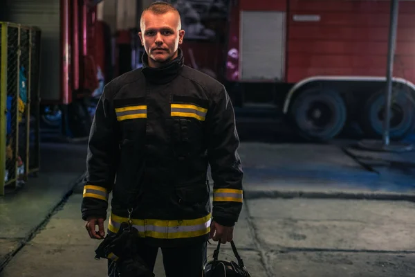 Portrét mladého hasiče stojícího v ohnivém statiu — Stock fotografie