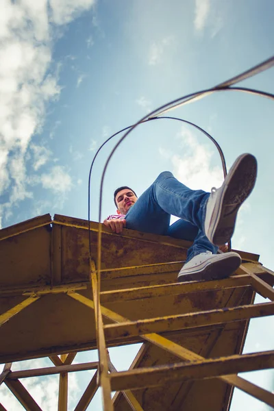 Jovem Está Sentado Alta Construção Ferro Olhando Frente Céu — Fotografia de Stock