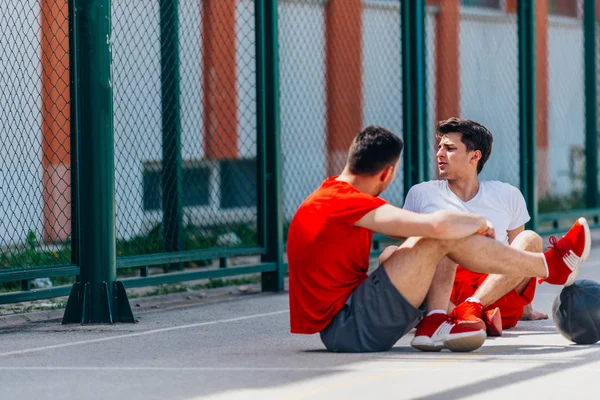 Dois Fortes Atletas Caucasianos Descansando Chão Quadra Basquete Enquanto Conversam — Fotografia de Stock