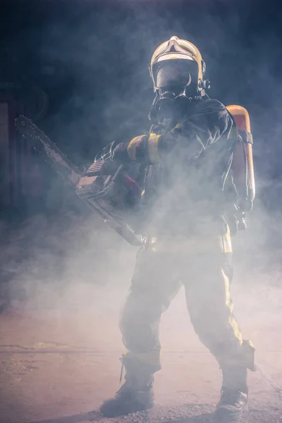 Portrait of young fireman standing and holding a chainsaw in the — Stock Photo, Image