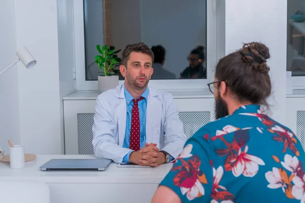 Un médico está hablando con un paciente hipster en el consultorio y le explica —  Fotos de Stock