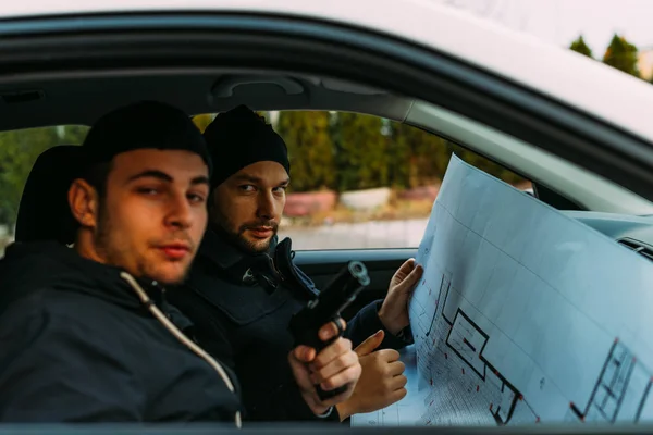 Zwei Diebe parkten in einem wartenden Verbündeten, während sie telefonierten, beobachteten ihr Ziel und luden ihre Waffen. — Stockbild Zwei Diebe parkten beim Telefonieren in einem wartenden Auto — Stockfoto