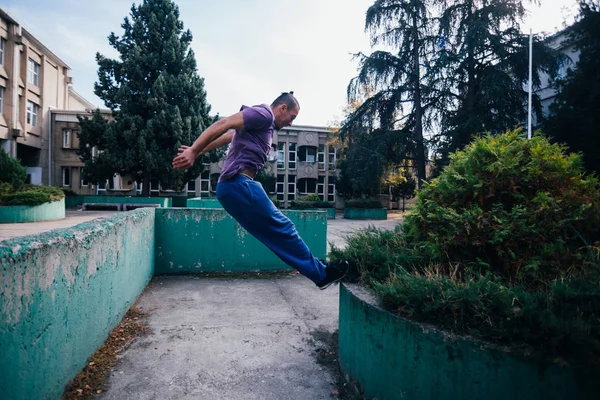 Young parkour guy jumping over a concrete wall and landing on an — Stock Photo, Image