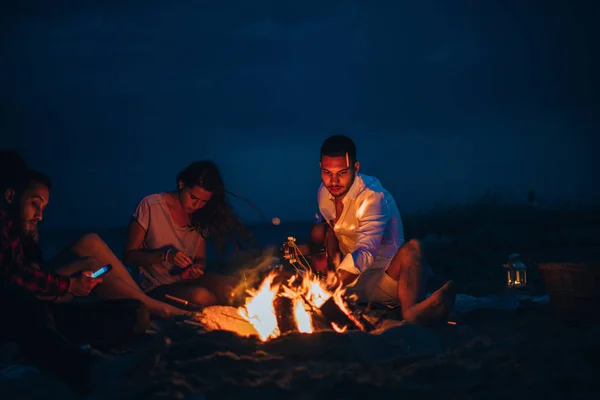 Amigos desfrutando de música perto da fogueira à noite na praia — Fotografia de Stock