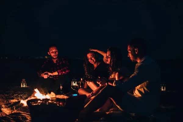 Gli amici erano seduti intorno al fuoco mentre bevevano birra e pla — Foto Stock
