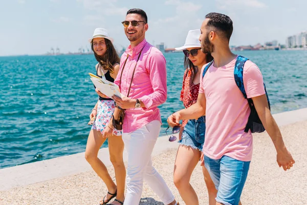 Quattro turisti a piedi vicino al mare durante la lettura di una mappa e de — Foto Stock