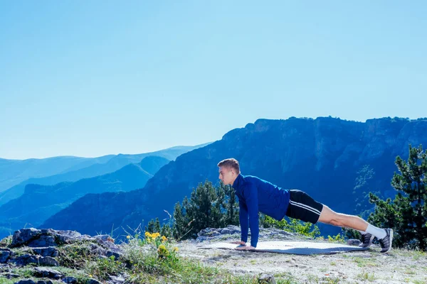 强壮英俊的金发运动员在山顶上做俯卧撑 同时欣赏山谷中湖面的迷人景色 — 图库照片