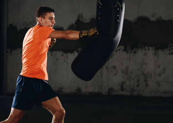 Silhouette male boxer hitting a huge punching bag at a boxing studio. Man boxer training hard