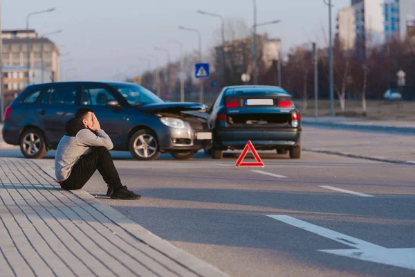 若い男が道路に座っていて 車の事故の後に揺れているのを見ている — ストック写真
