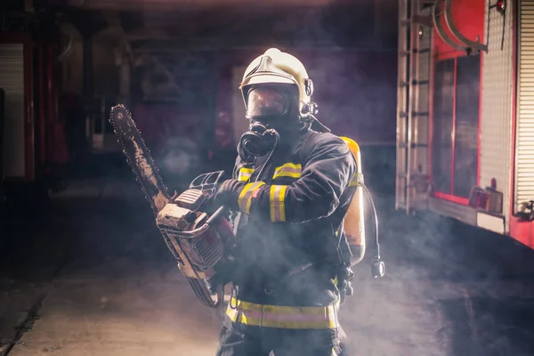 Retrato do jovem bombeiro de pé e segurando uma motosserra no — Fotografia de Stock