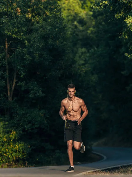 Sport and fitness runner man with headphones running on road training for marathon run doing high intensity interval training sprint workout outdoors in summer